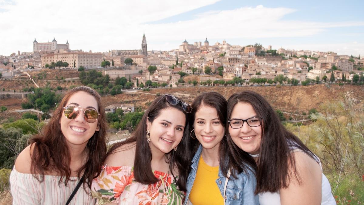 four young women smile with an old spanish town visible in the distance 