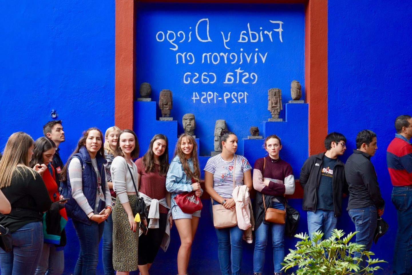 a line of Trinity students in front of a blue wall with Spanish writing